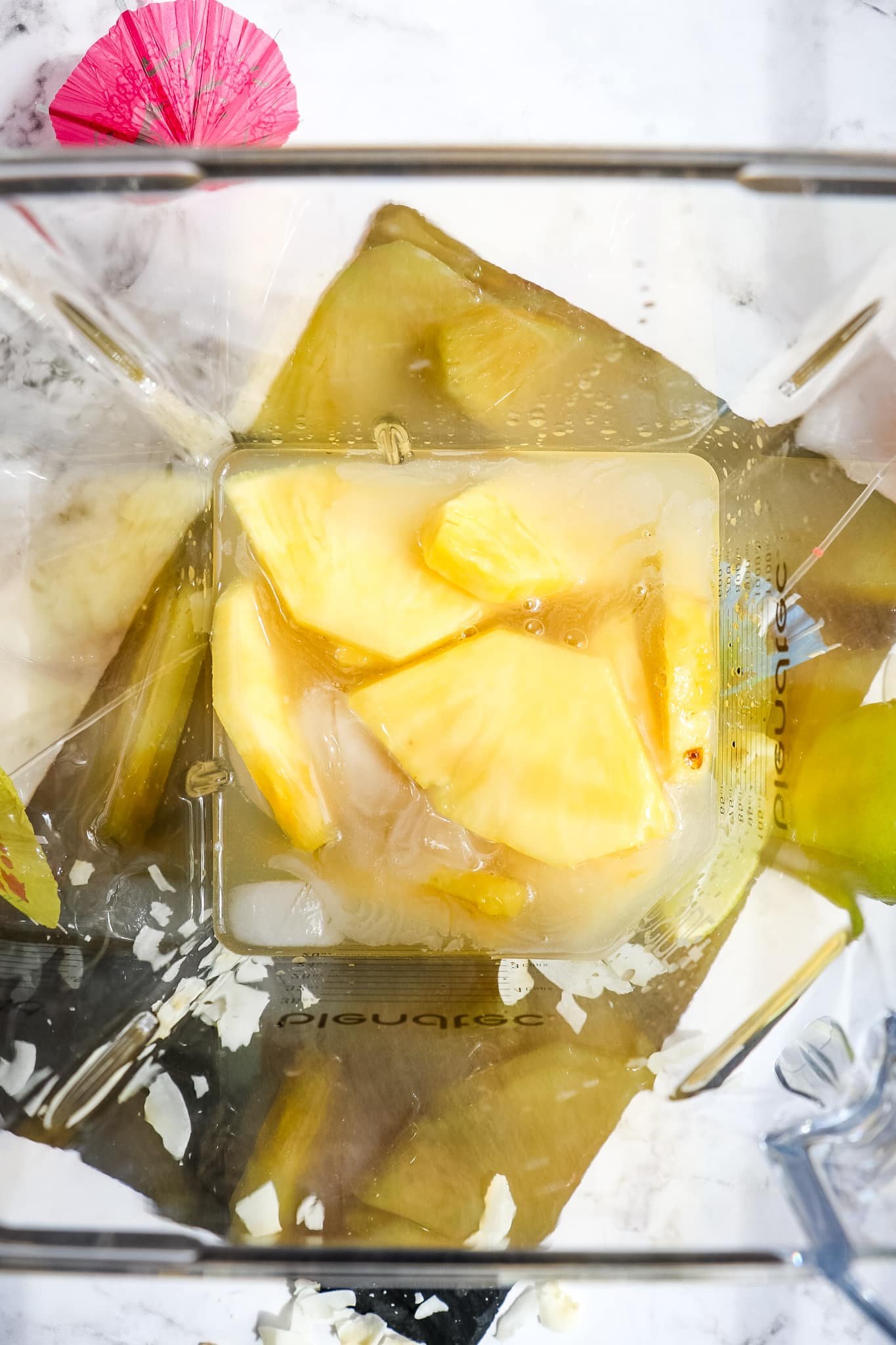 Ingredients for a frozen pineapple daiquiri in a blender, looking down into jar.