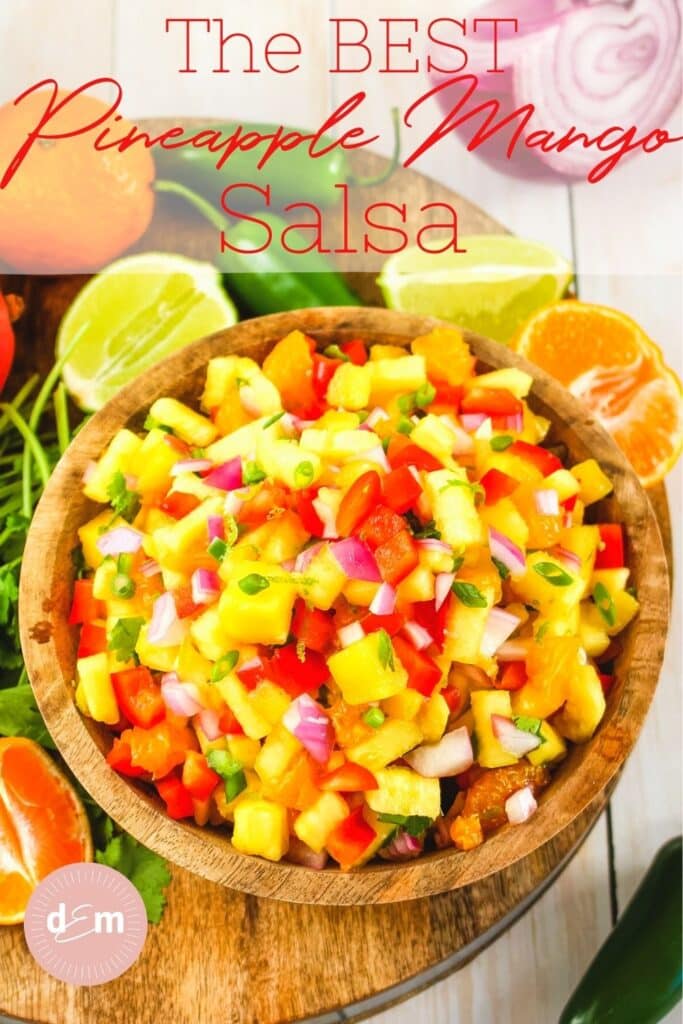 Fresh pineapple mango salsa in bowl, garnished with limes and oranges.