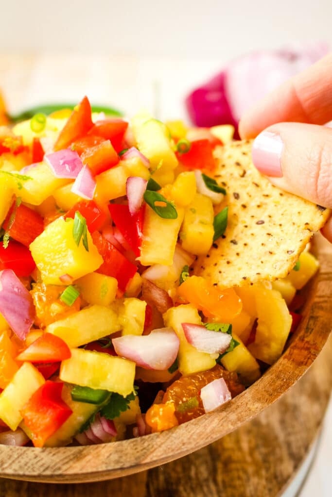 Pineapple mango salsa being scooped with a chip.