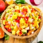 Pineapple mango salsa in bowl, garnished with oranges and peppers on the side.