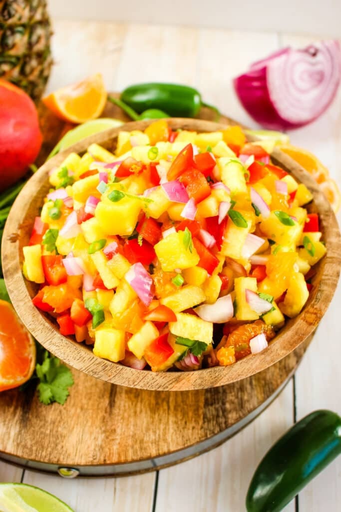 Pineapple mango salsa in bowl, garnished with oranges and peppers on the side.