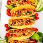 Rotisserie chicken tacos with avocado slices, cherry tomatoes and limes.