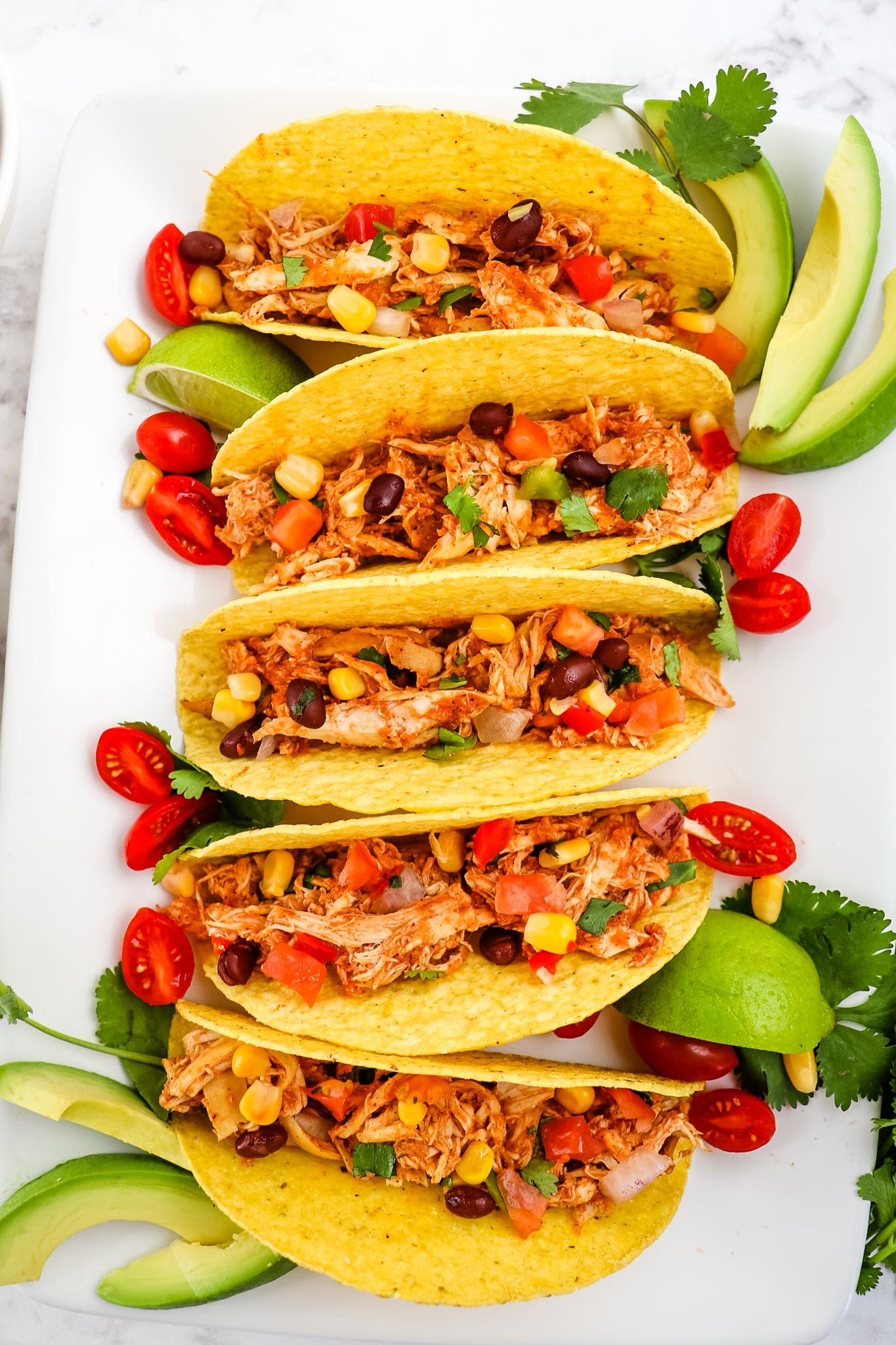 Rotisserie chicken tacos with avocado slices, cherry tomatoes and limes.