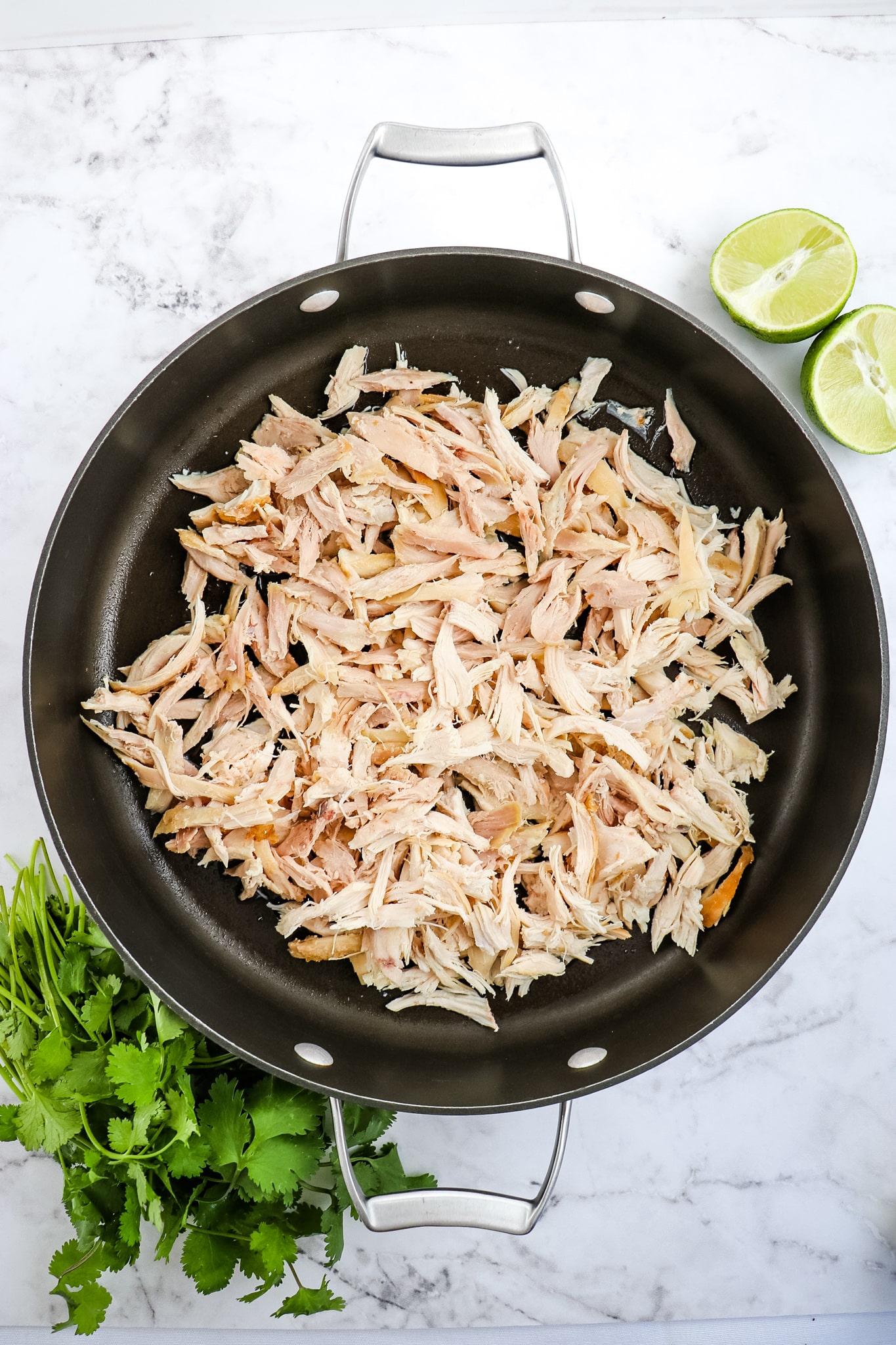 Shredded chicken in a large skillet with water. Limes on the side.