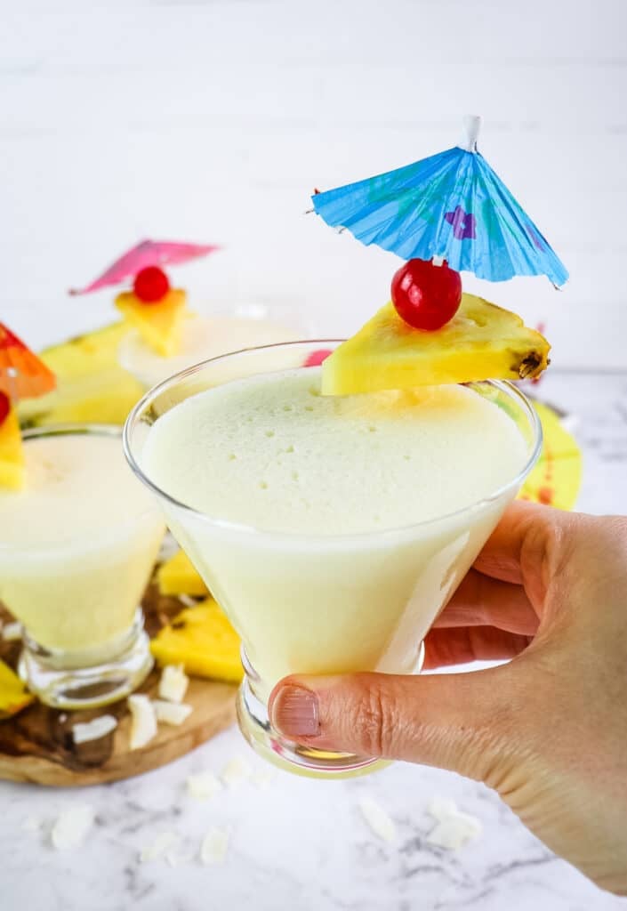 Skinny malibu pina colada being held in hand, with little umbrella garnish with cherry and pineapple.