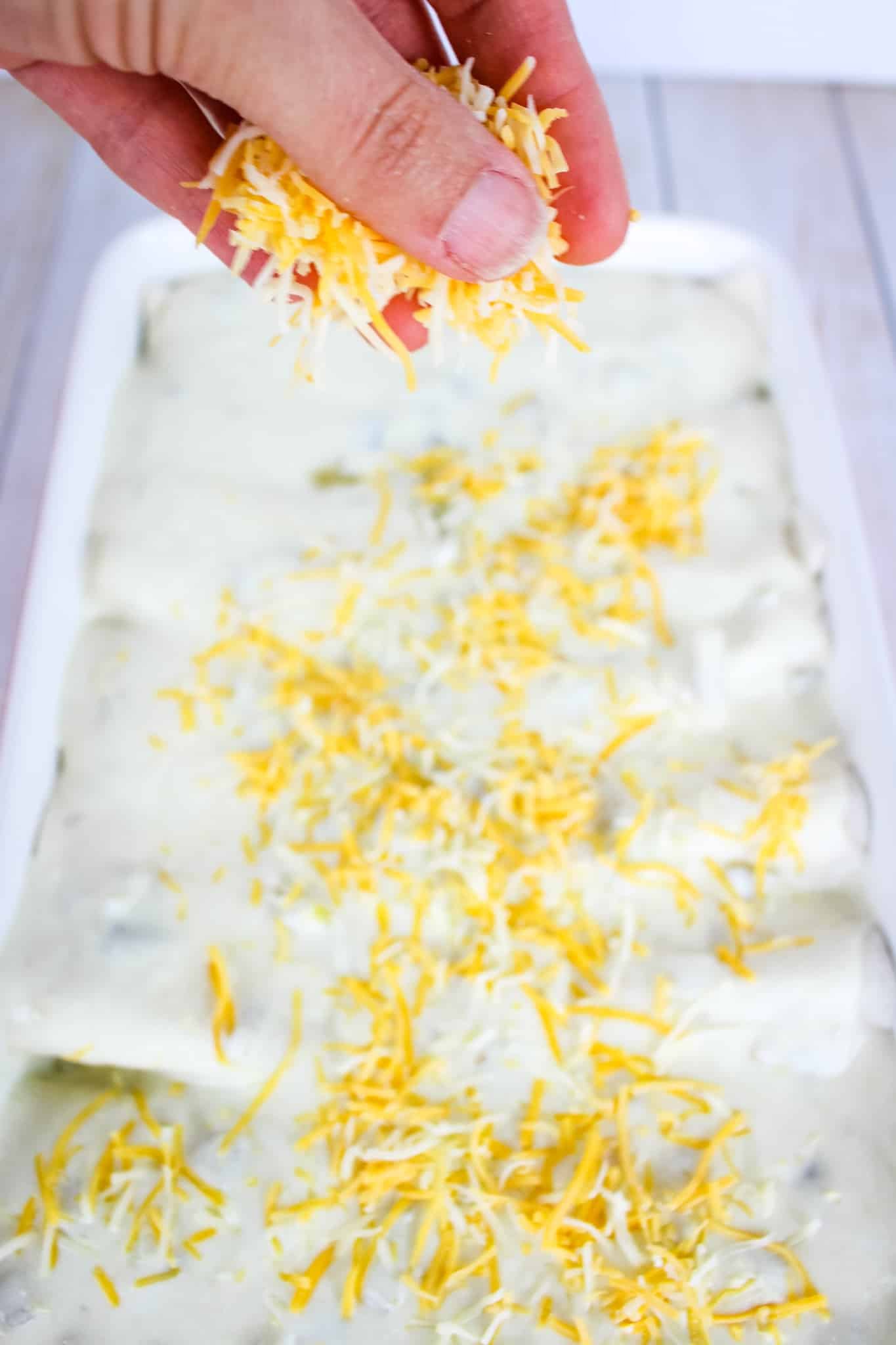 Sprinkling top of sour cream enchiladas with shredded cheese.