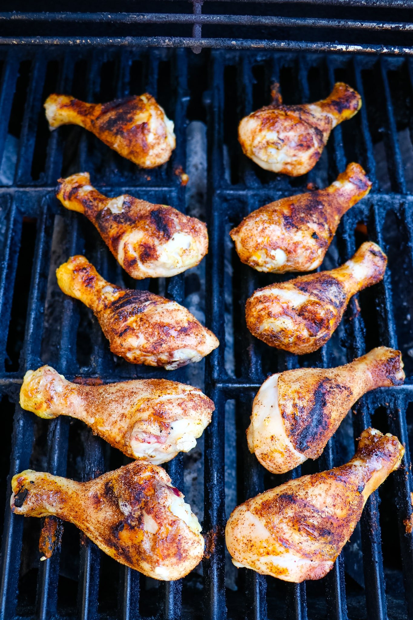 Ten seasoned chicken legs cooking on the grill.