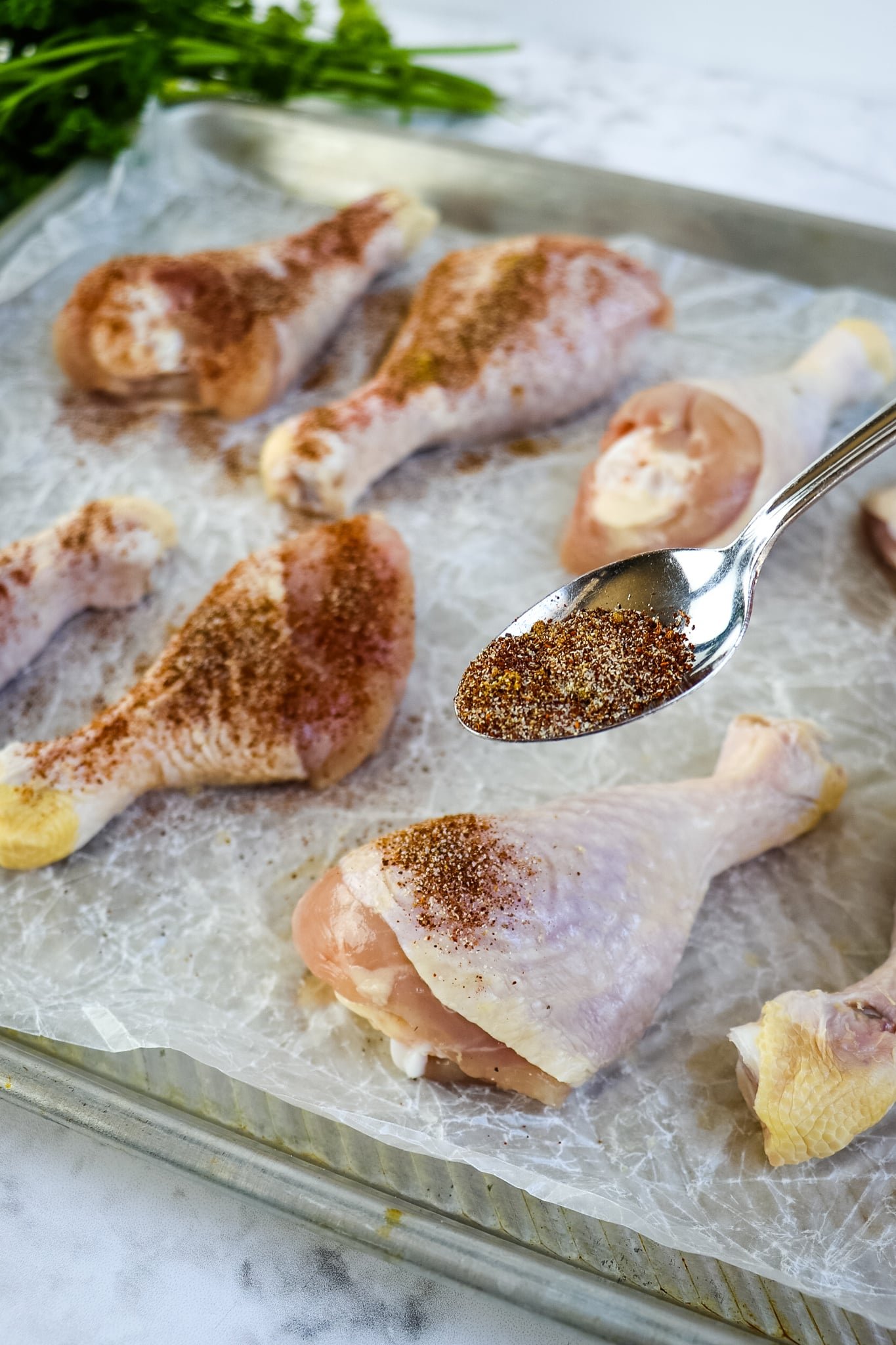 Seasoning being added to chicken legs on a sheetpan.