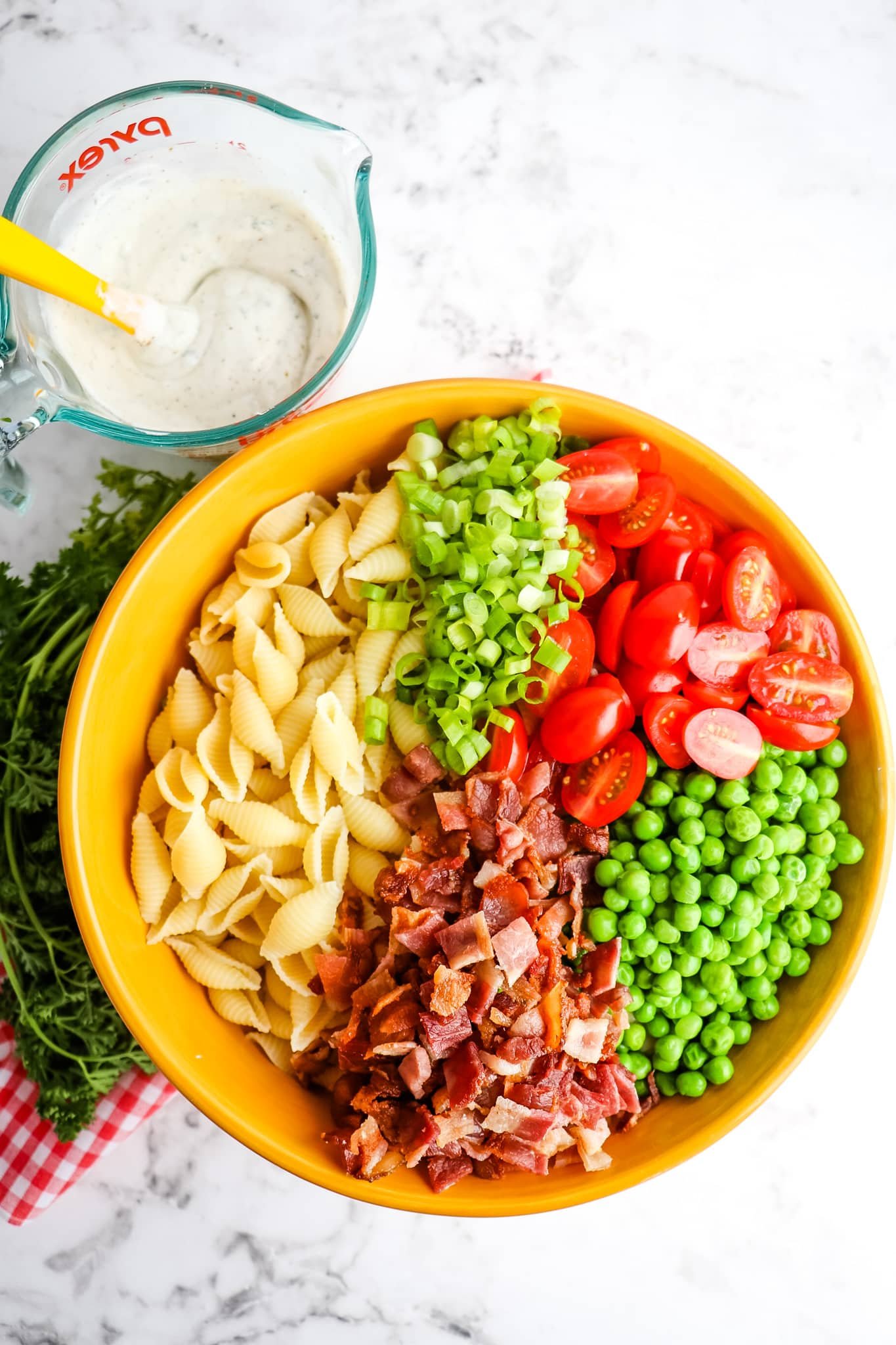 Ingredients of pasta salad in bowl, with dressing on the side.