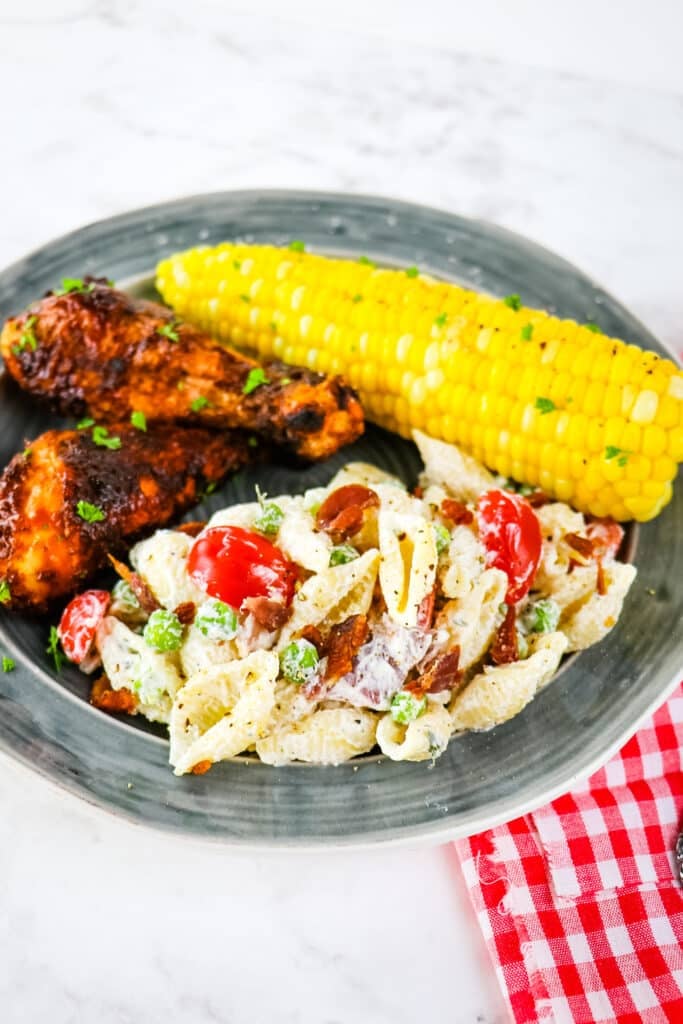 Plate with bbq chicken, corn on the cob and bacon ranch pasta salad.