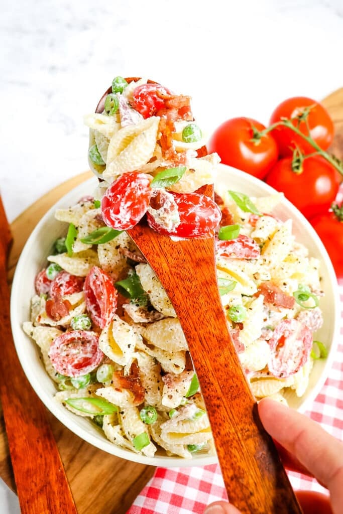 Pasta salad in white bowl, with wooden spoon of salad serving.
