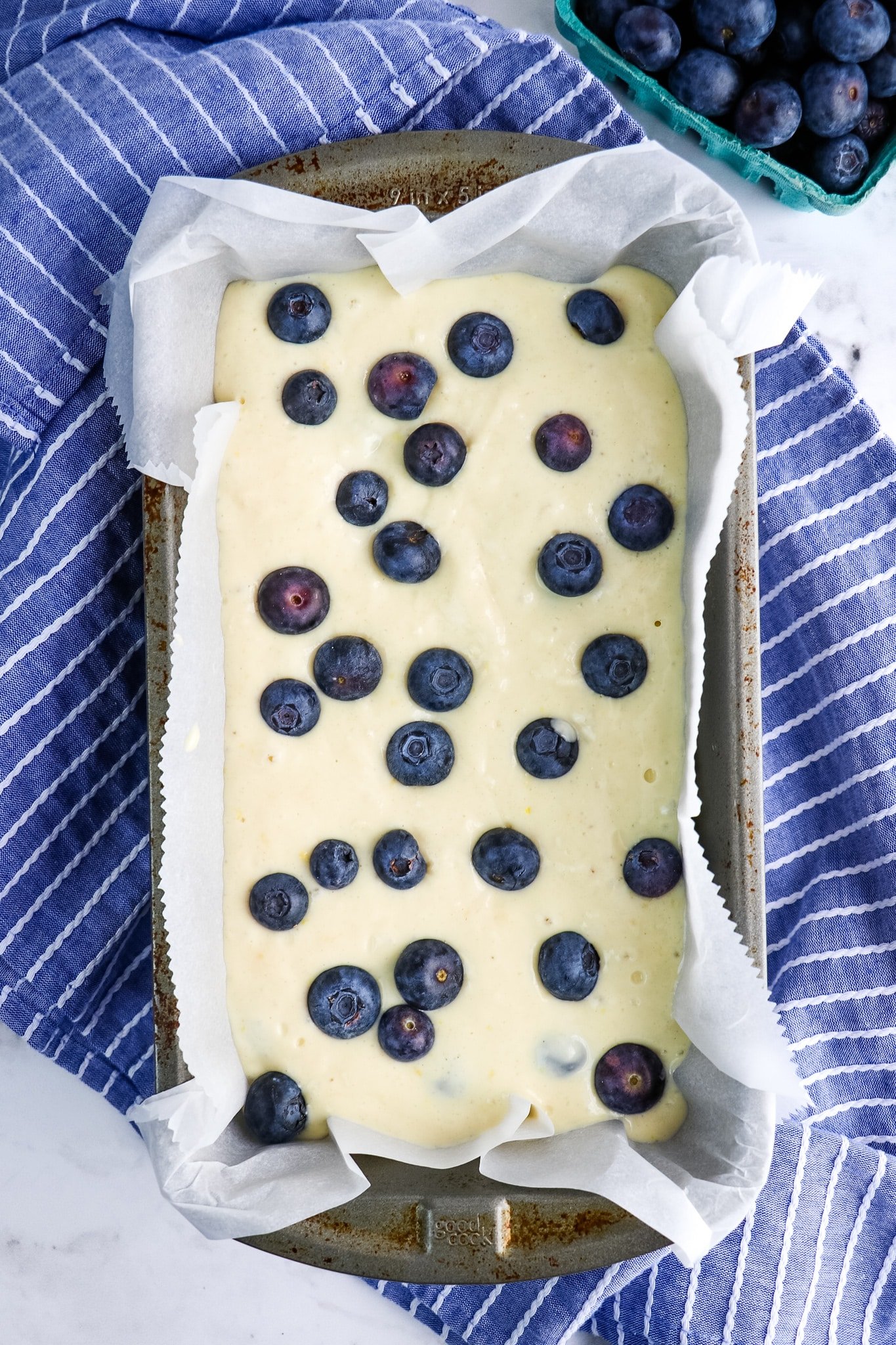 Lemon blueberry batter in loaf pan, topped with fresh blueberries.