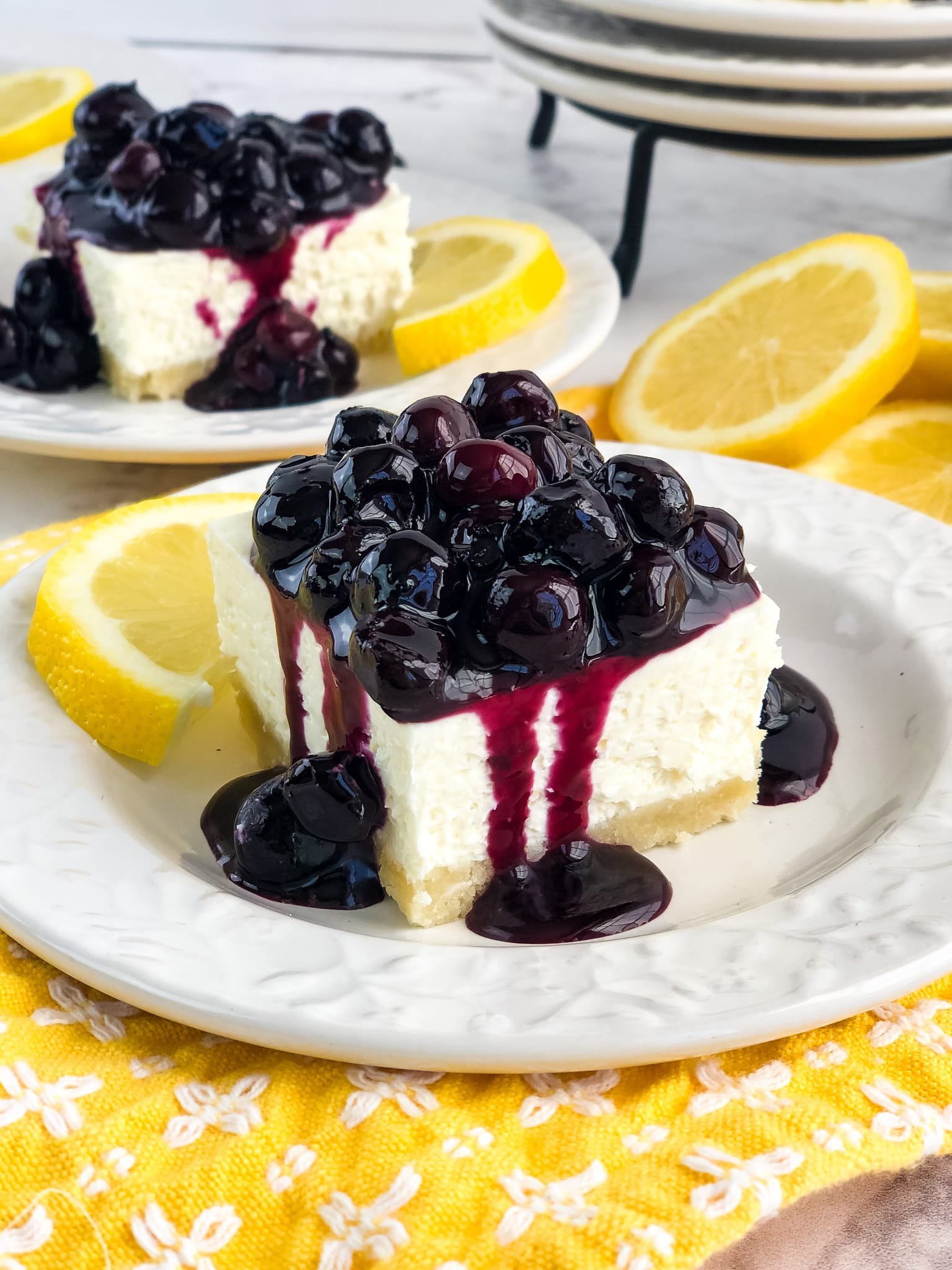 Slice of lemon blueberry cheesecake on plate, topped with blueberry topping, garnished with lemons.