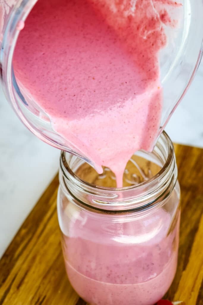 Raspberry smoothie being poured into a mason jar.