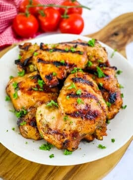 Grilled boneless skinless chicken thighs on plate, sprinkled with chopped parsley.