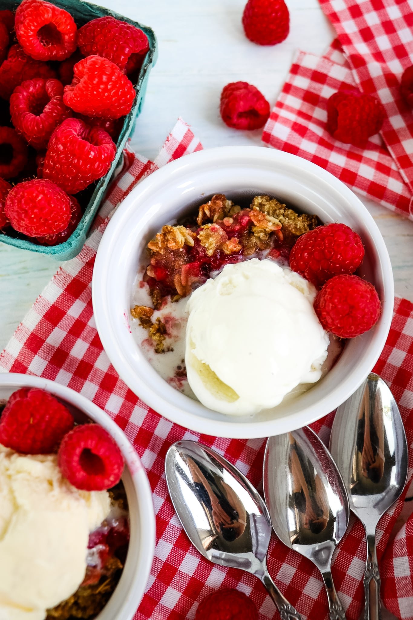 Single dish of raspberry crumble topped with ice cream and fresh raspberries.
