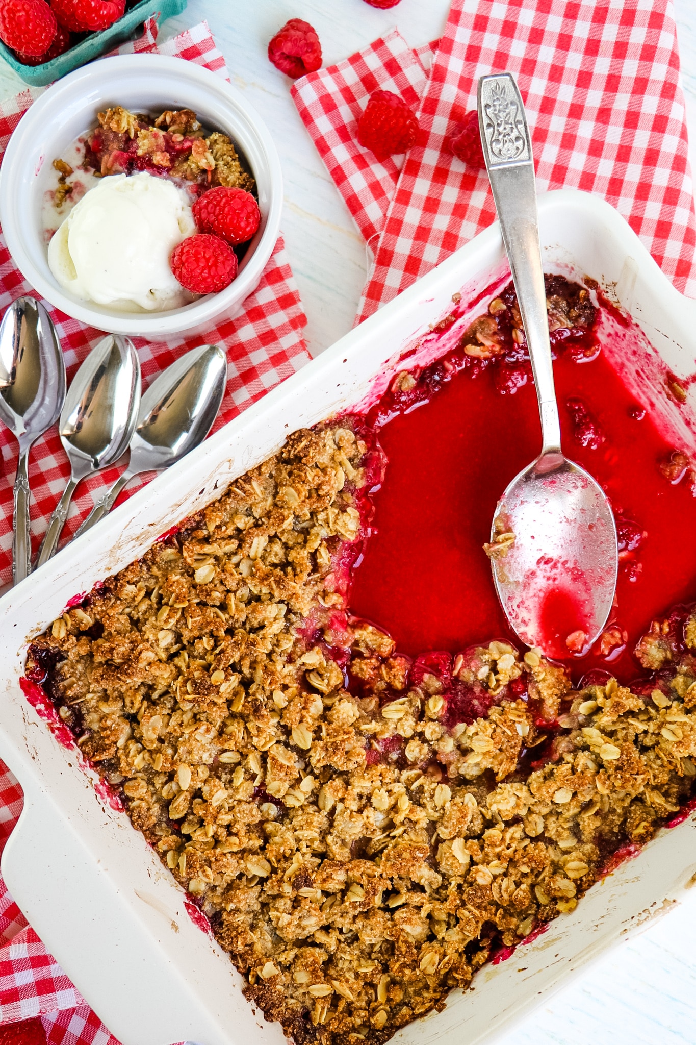 Raspberry crumble spooned out of dish, with bowl of crumble and ice cream on the side.