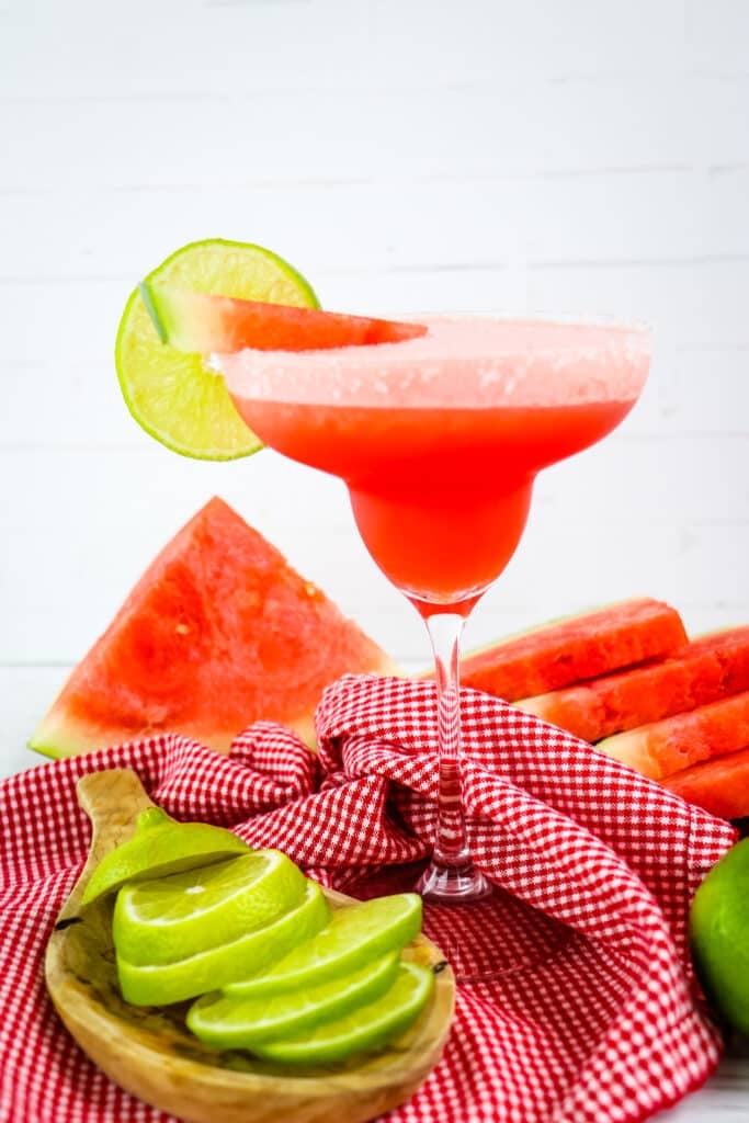 Frozen watermelon margarita, in margarita glass with limes and watermelon on the side.
