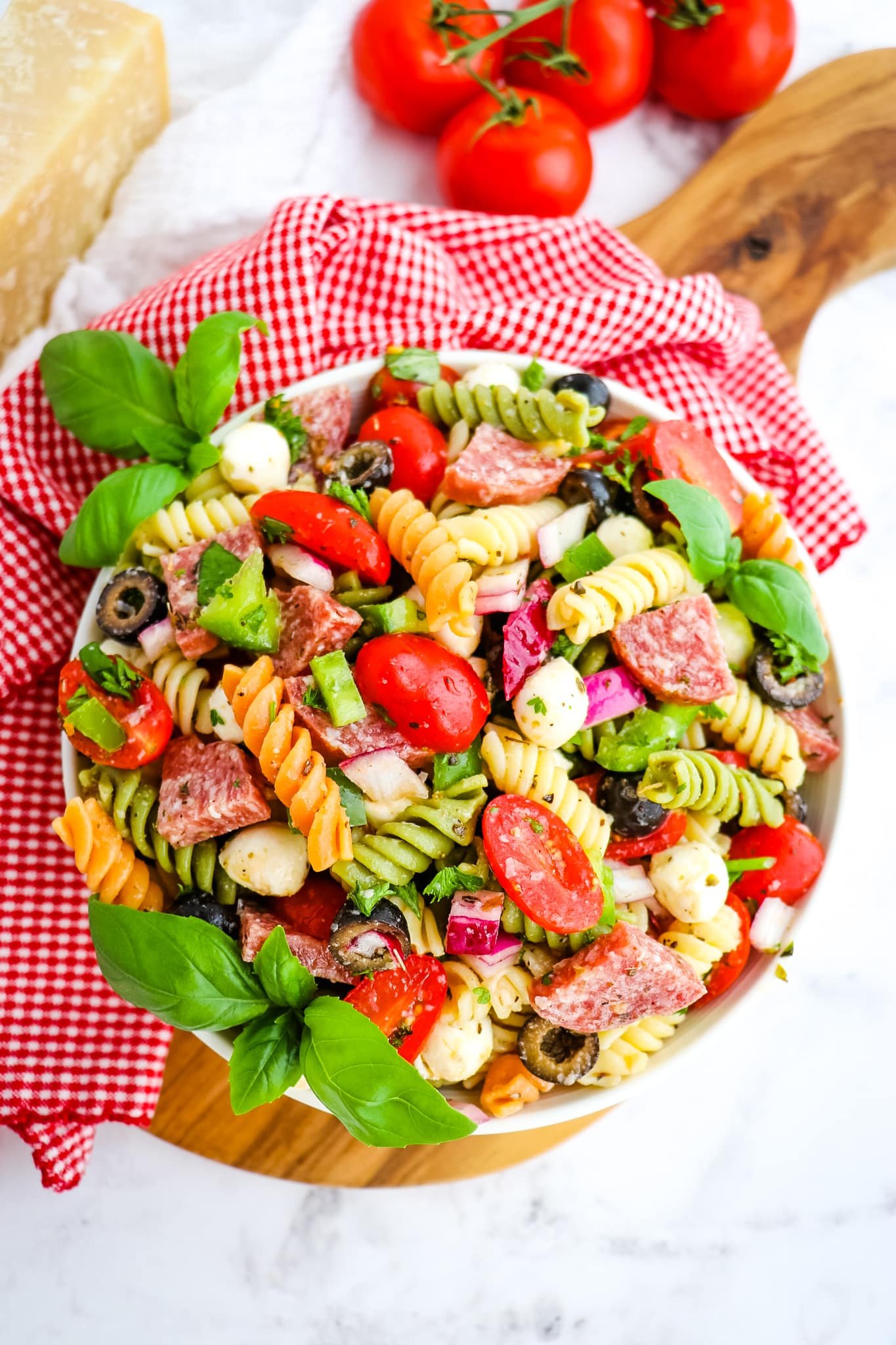Italian pasta salad in bowl, garnished with tomatoes and fresh basil leaves.
