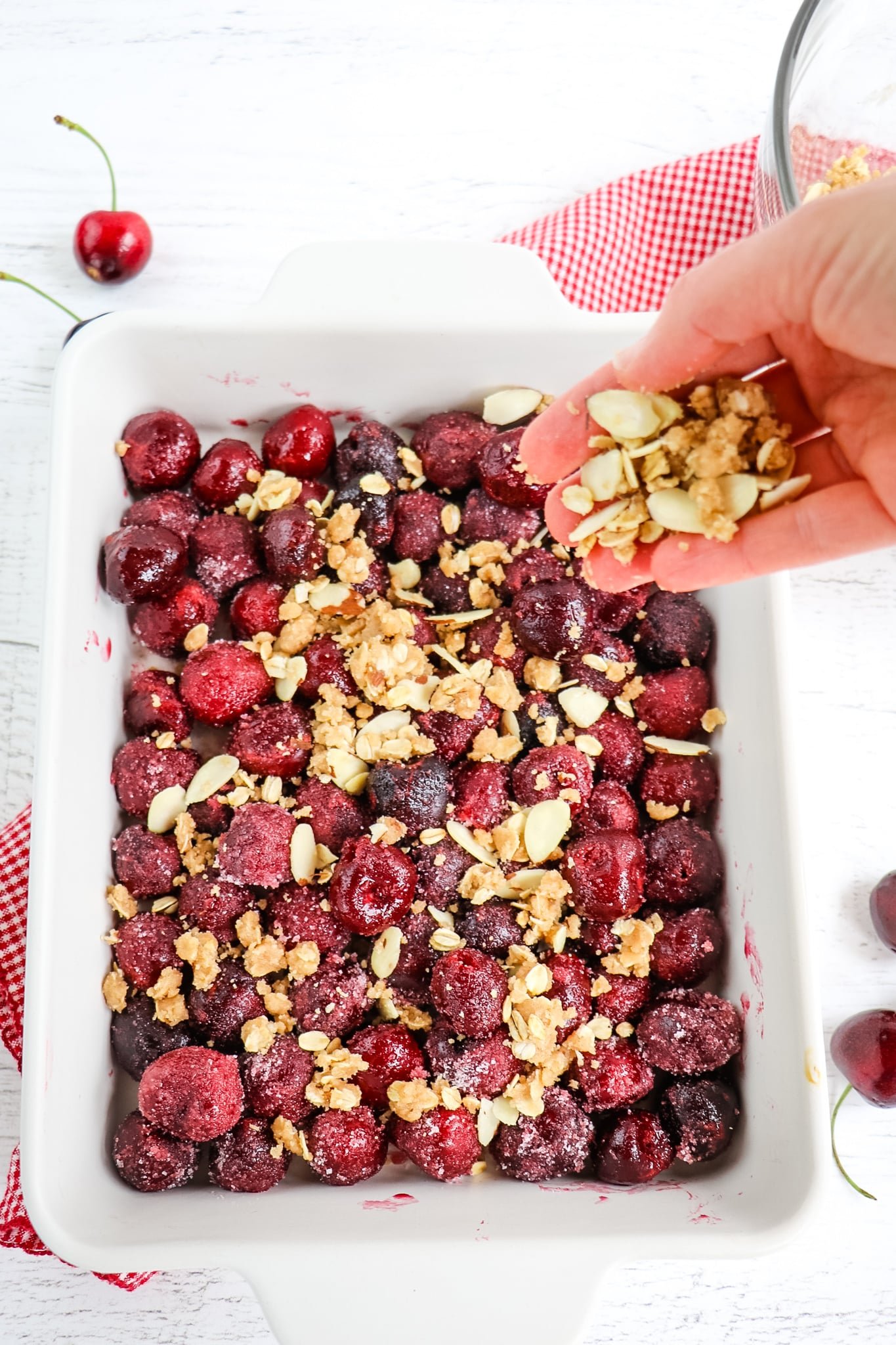 Sprinkling almond crumble over top of cherries in baking dish.