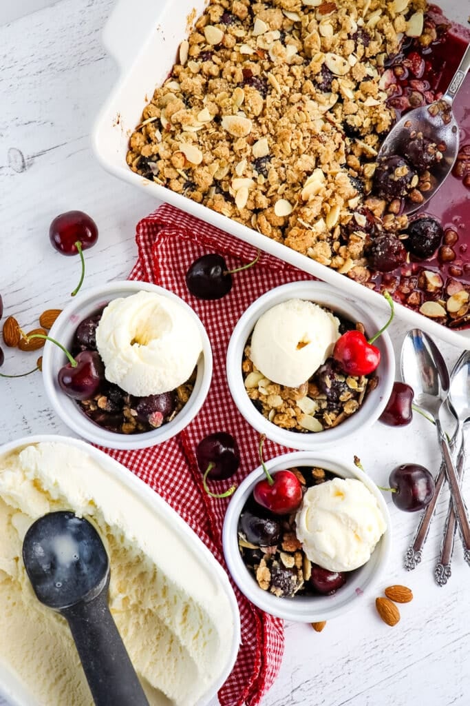 Cherry crisp served in three bowls, topped with vanilla ice cream.