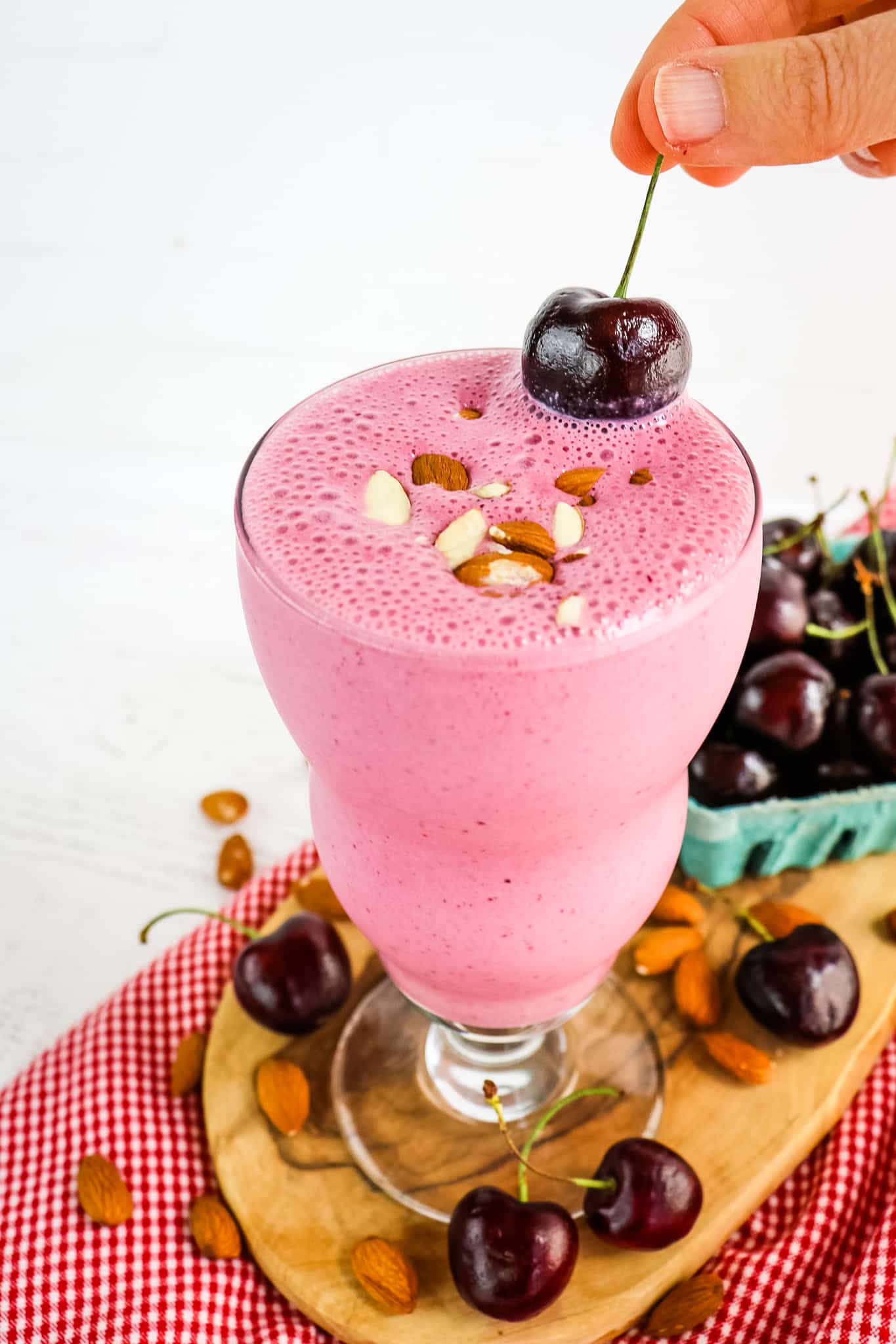 Cherry smoothie being topped with a cherry and sliced almonds.