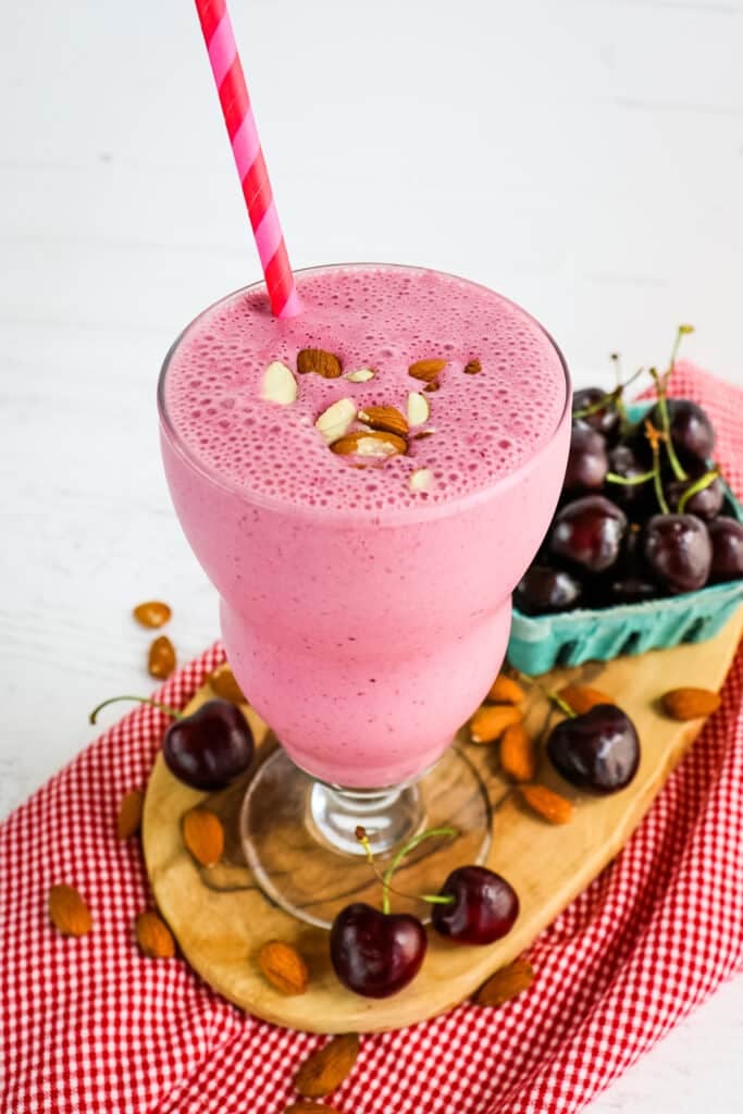 Almond and cherry smoothie in glass with straw, cherries on the side.