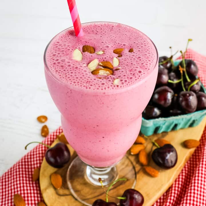Almond and cherry smoothie in glass with straw, cherries on the side.