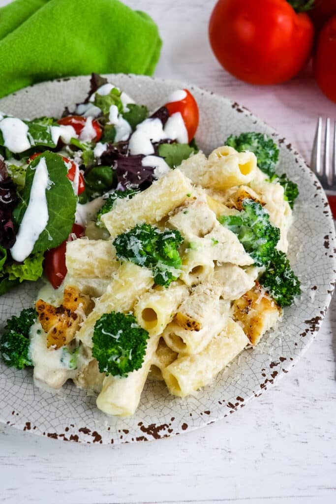 Chicken and broccoli alfredo on plate with side salad.