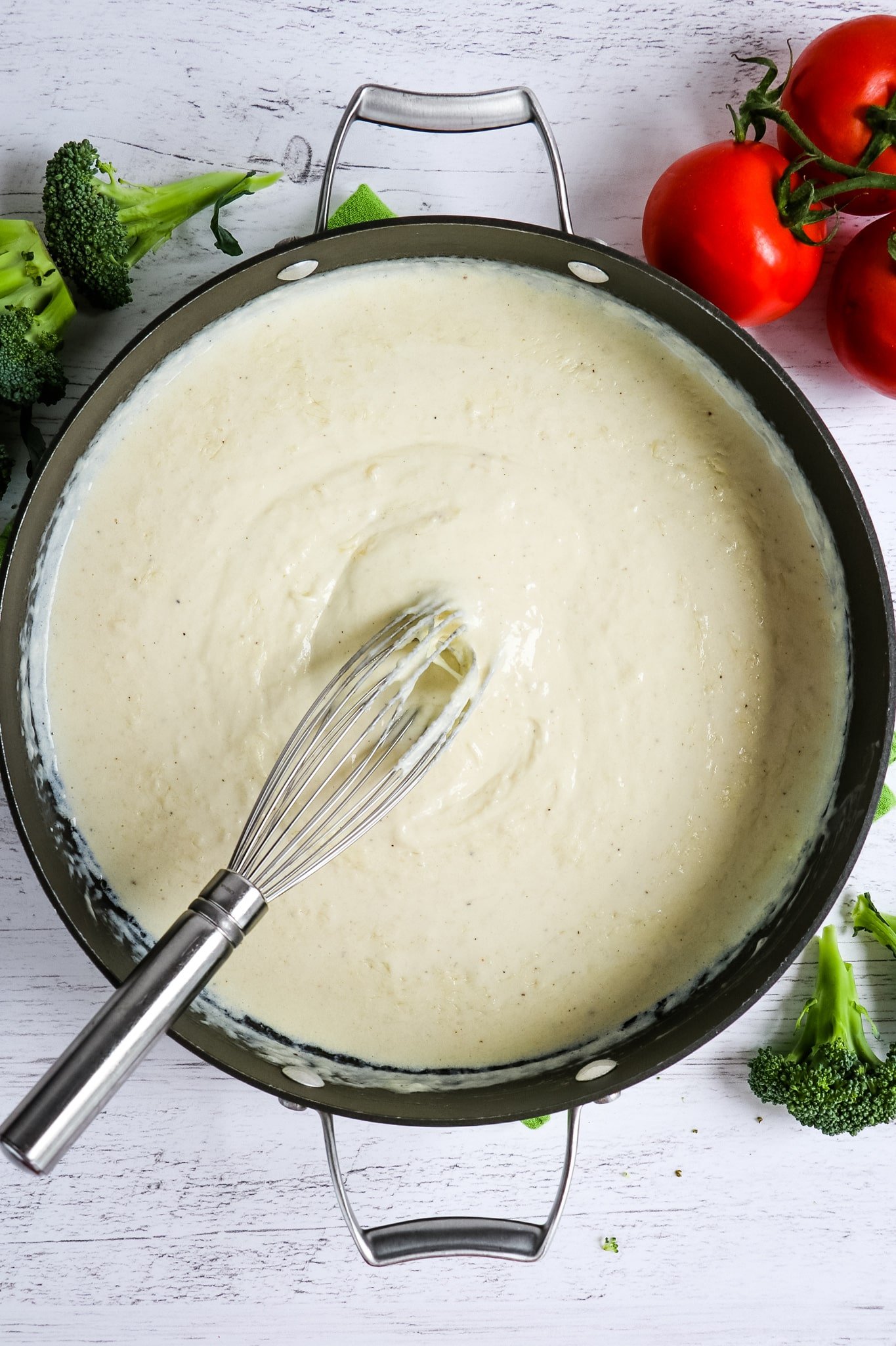 Homemade alfredo sauce in skillet with whisk in the middle.