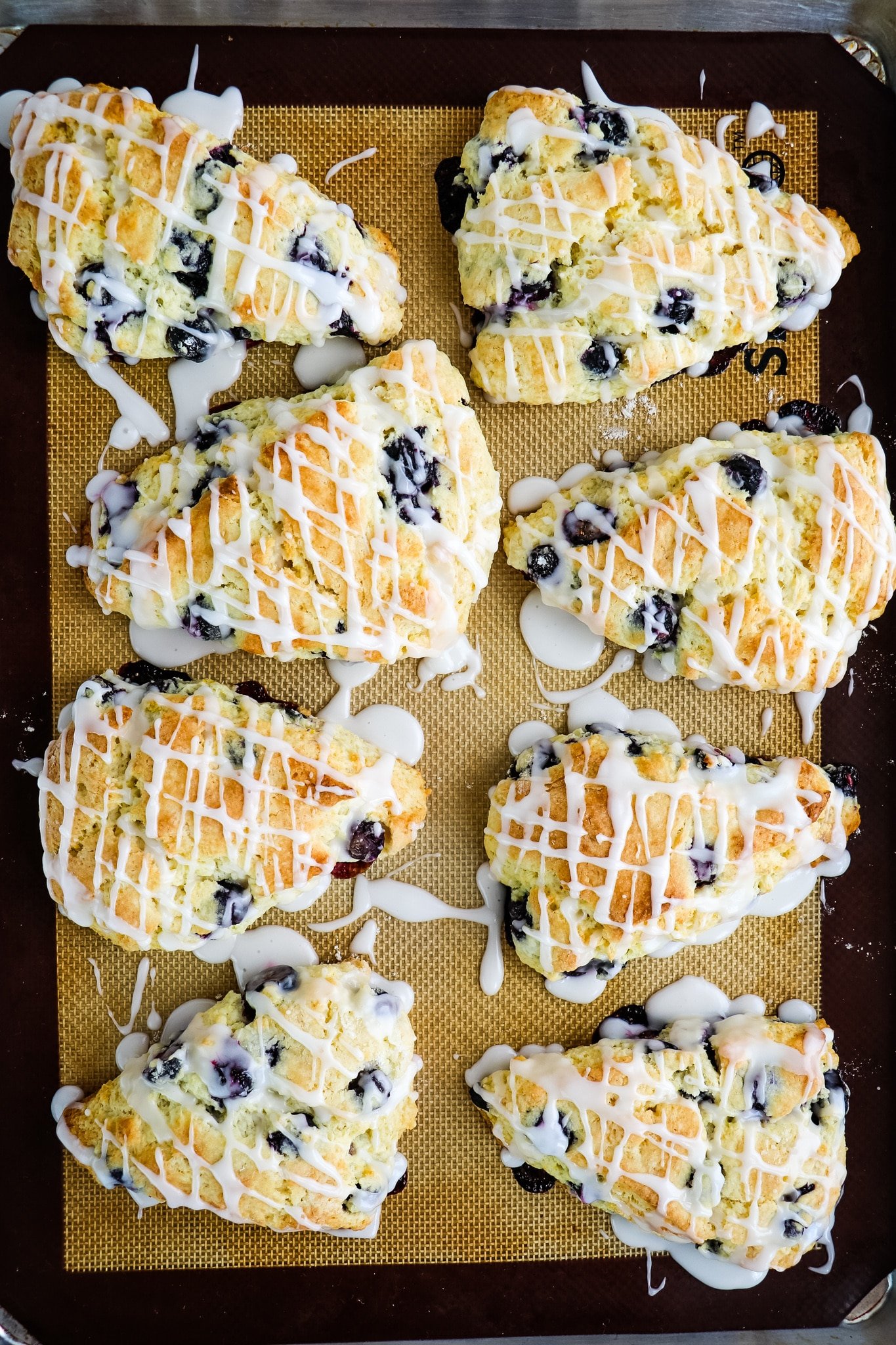Glazed lemon blueberry scones on baking sheet.