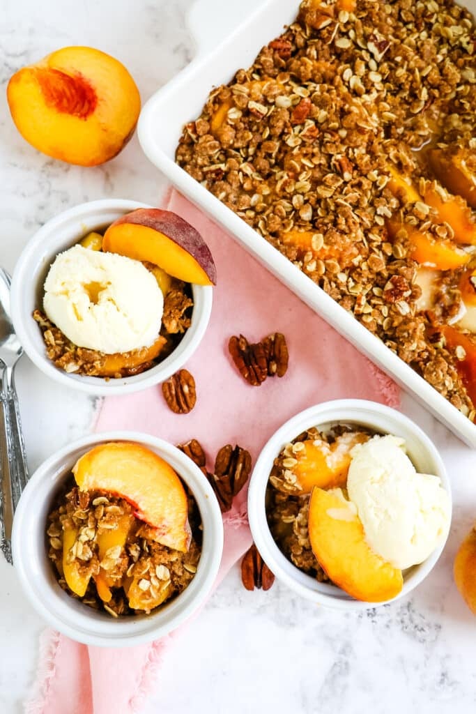 Healthy peach crisp in baking dish and three serving bowls.
