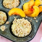 Peach muffins in muffin tin with sliced peaches on the side.