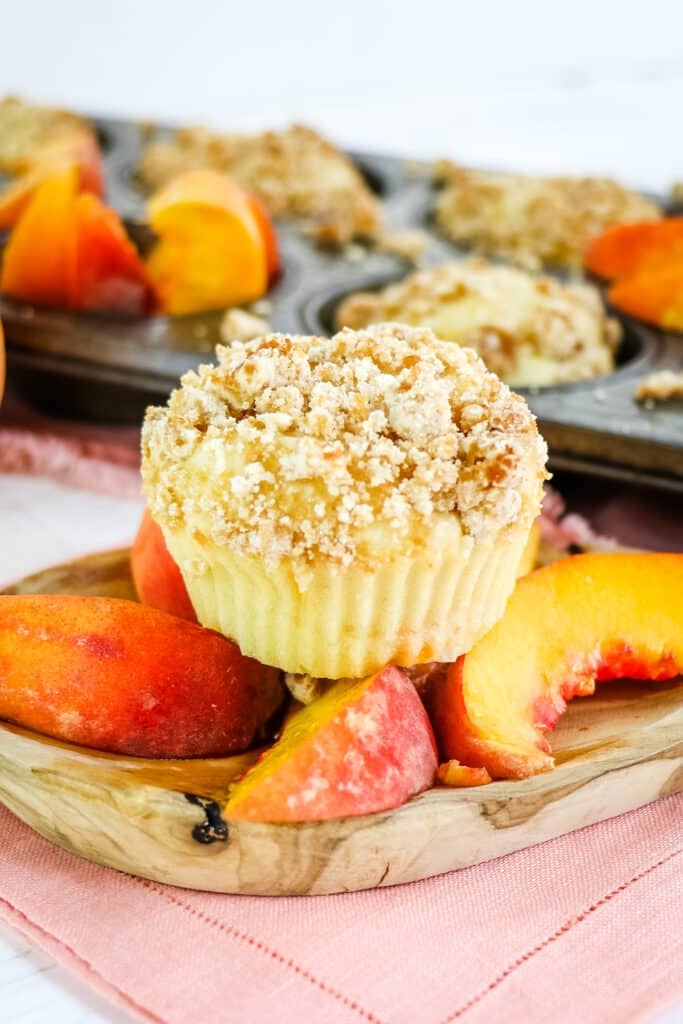 Single peach muffin sitting on top of sliced peaches.