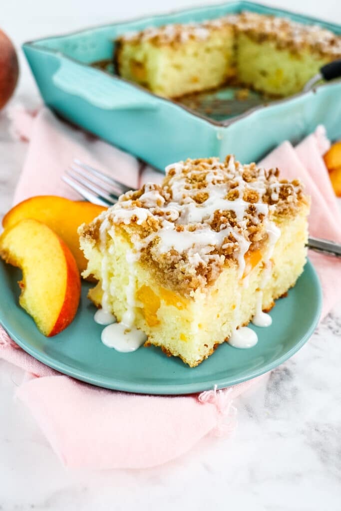 Slice of peach coffee cake on blue plate with peach slices on the side.