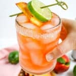 Peach margarita, garnished with peach and lime slices, held in hand.