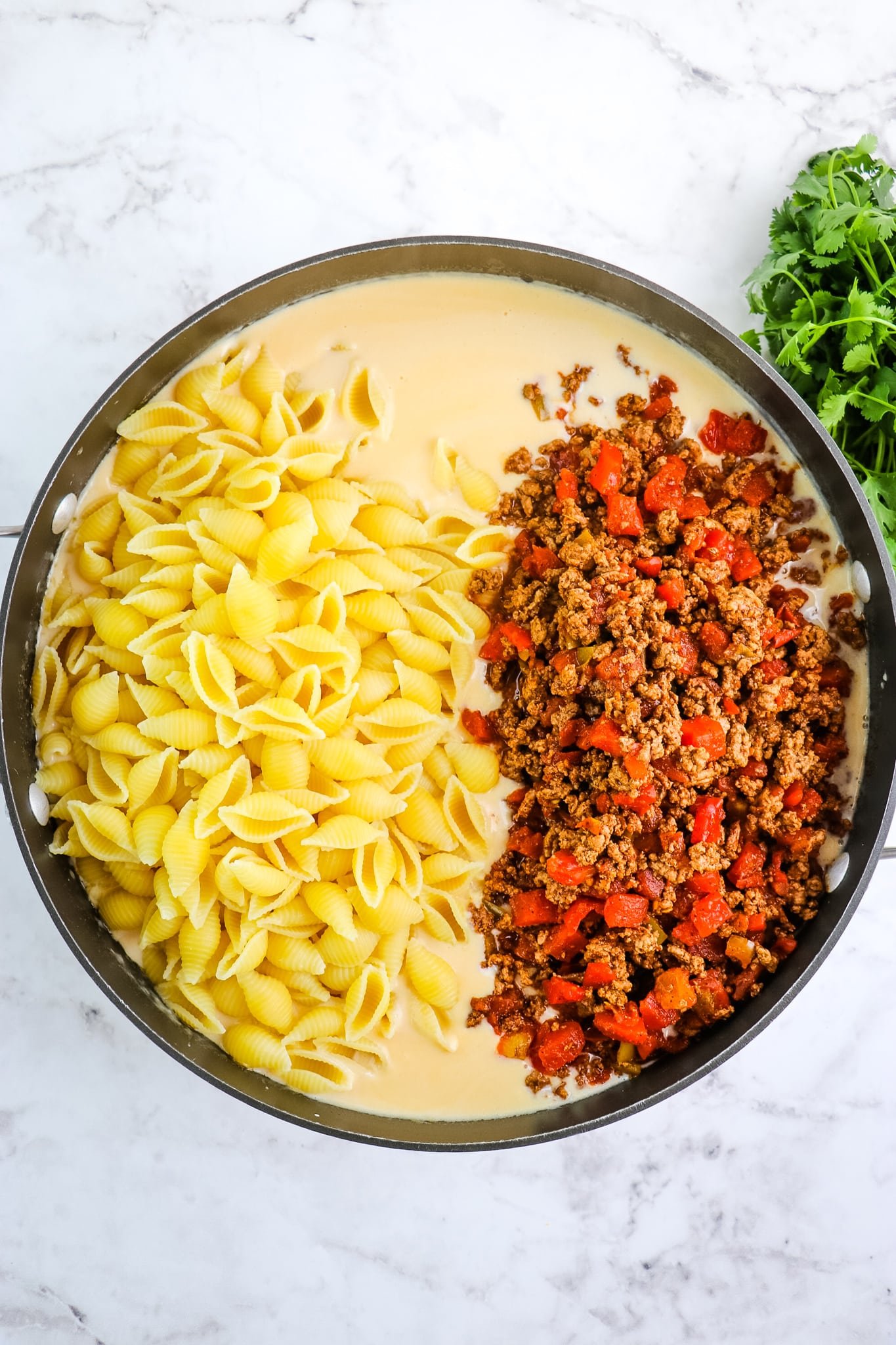 Cheese sauce, pasta and seasoned ground beef in skillet for taco mac and cheese.