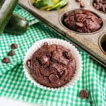 Chocolate zucchini muffin on a green napkin with muffins and zucchini in the background.