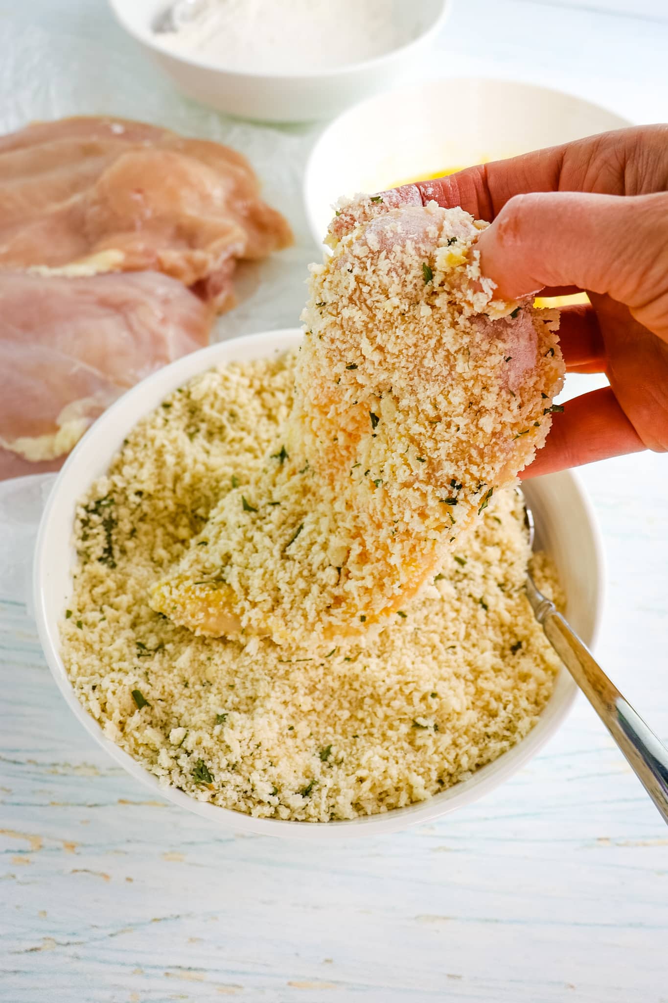 Chicken breast being dipped in Parmesan coating.