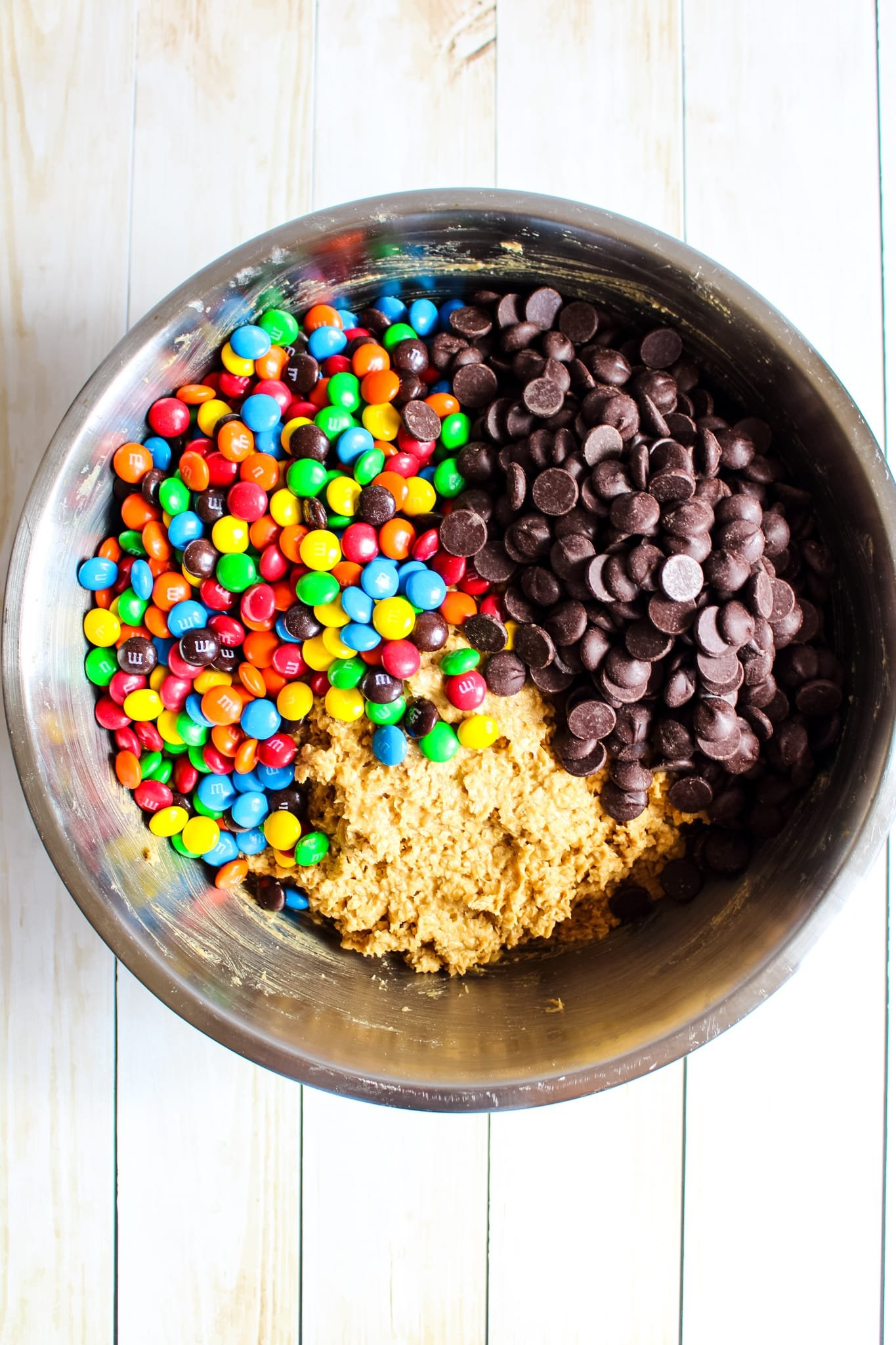 Monster cookie recipe of cookie dough in bowl with m&m's and chocolate chips on top.