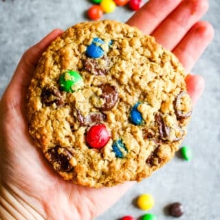 Large monster cookie held in hand, with M&M candies in the background.