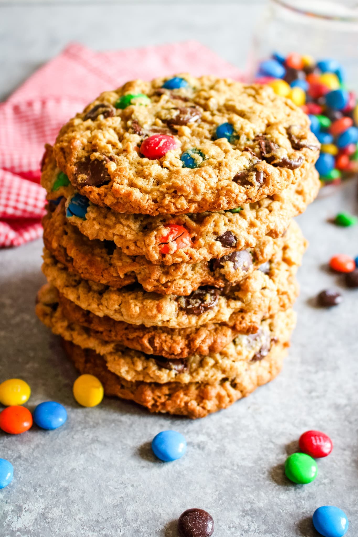 Large stack of monster cookies with M&M's in jar in background.