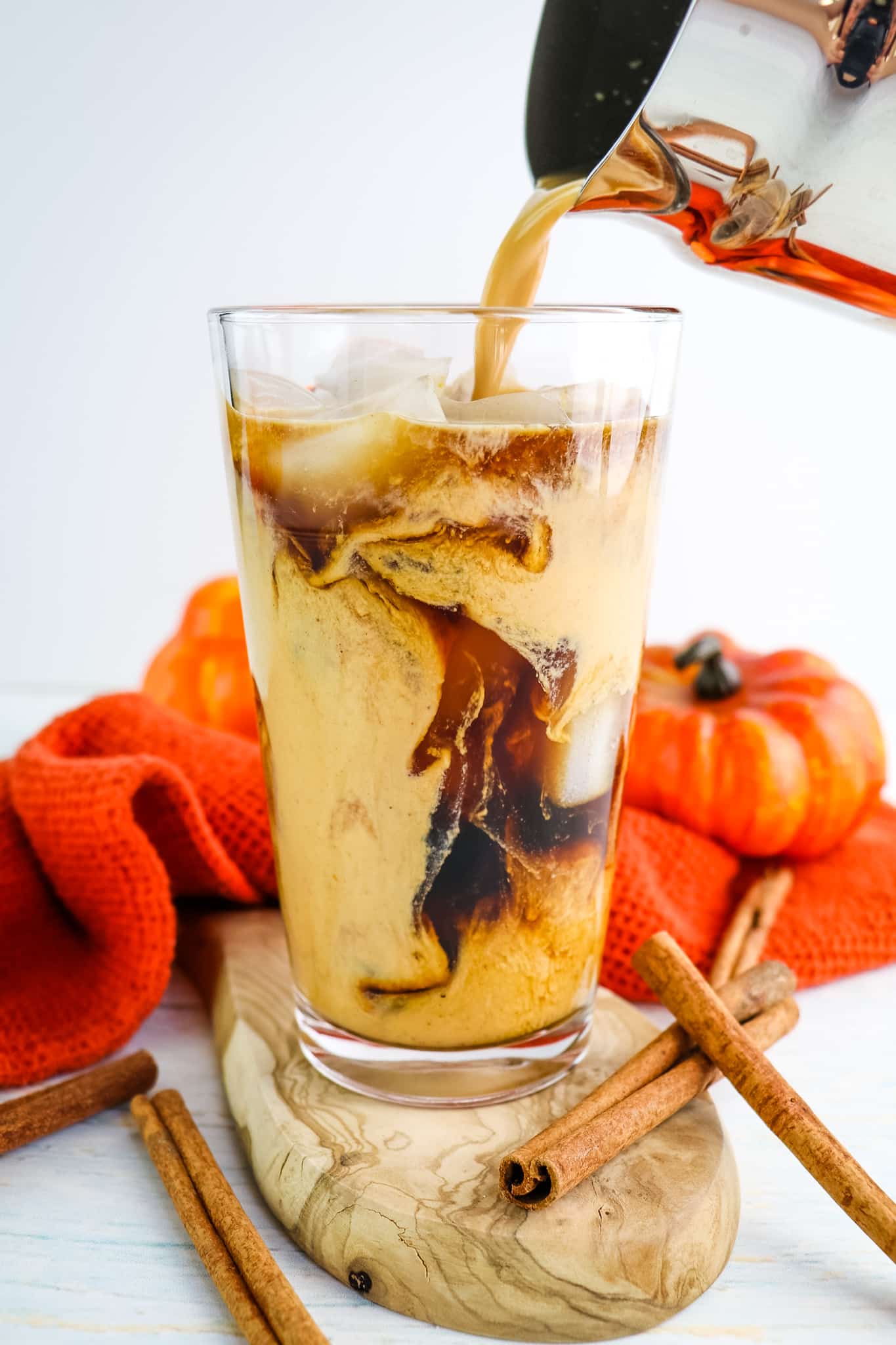 Pumpkin spice cold brew on ice with pumpkin cream being poured into glass.