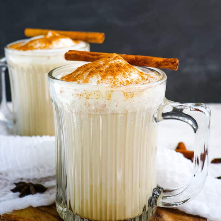 Two chai tea lattes in mugs topped with cinnamon sticks.