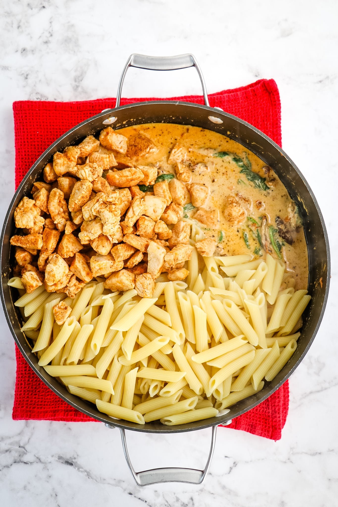 Creamy tuscan chicken sauce with pasta and diced chicken in skillet.