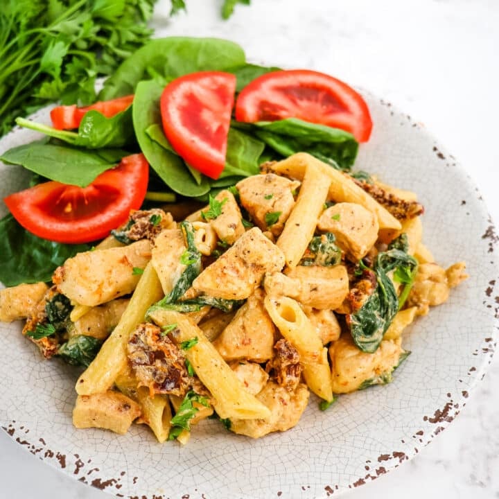 Creamy Tuscan chicken pasta on plate with spinach and tomato salad.
