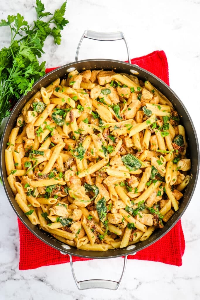 Finished creamy tuscan chicken pasta in skillet with parsley on the side.