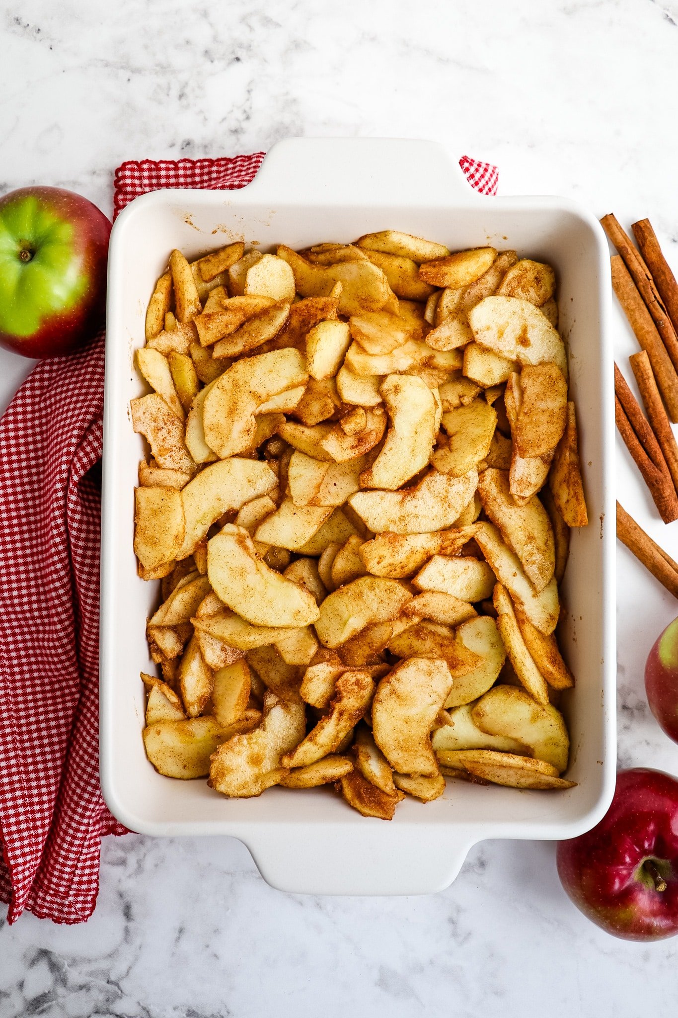 Sliced apples coated in brown sugar and cinnamon in baking dish.