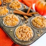 Pumpkin muffins in muffin tin with cinnamon sticks on the side.