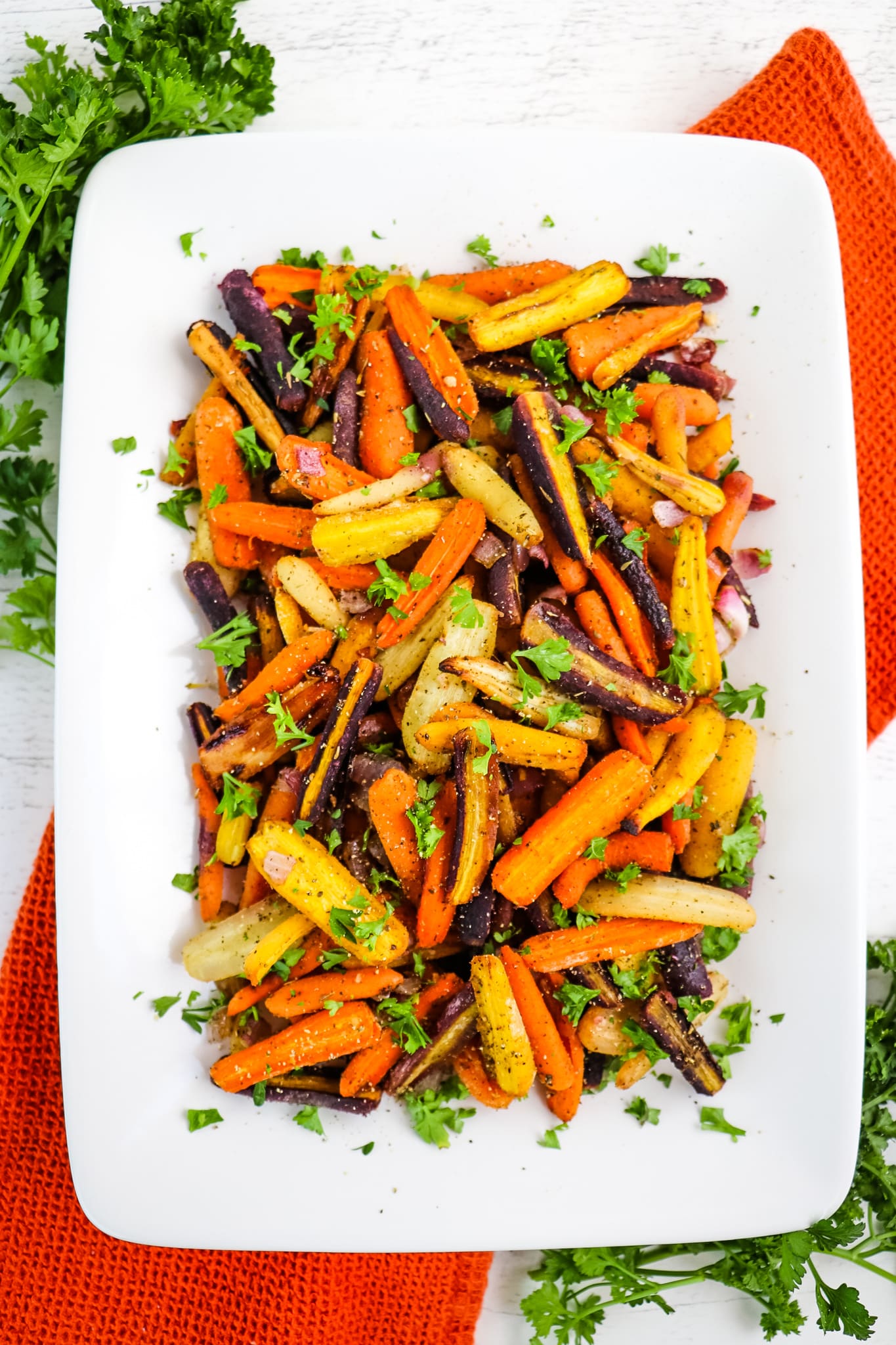 Roasted rainbow carrots on white platter topped with chopped parsley.
